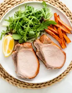 Plated Chuleta de Sajonia cooked in air fryer, juicy and with grill marks, served with fresh salad and air-fried potatoes. Receta rápida sin aceite