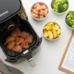 Guía de tiempos para freidora de aire con una tabla y alimentos crudos como pollo y patatas.
