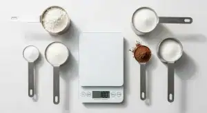 Tabla de equivalencias de tazas a gramos con ingredientes de repostería y una balanza de cocina.